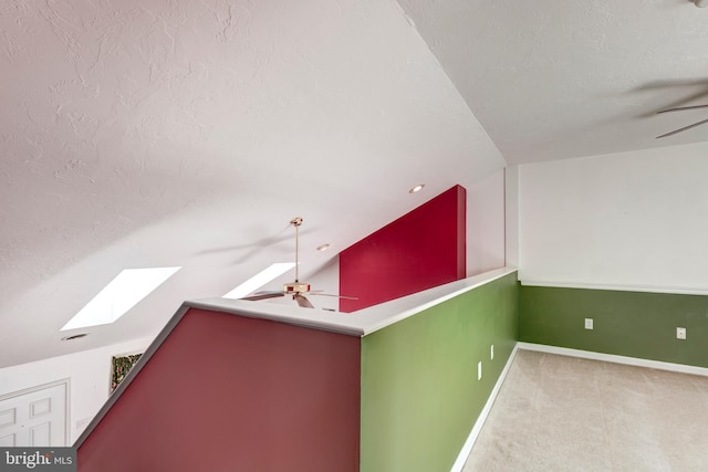 interior space featuring lofted ceiling with skylight, baseboards, carpet floors, and a textured ceiling