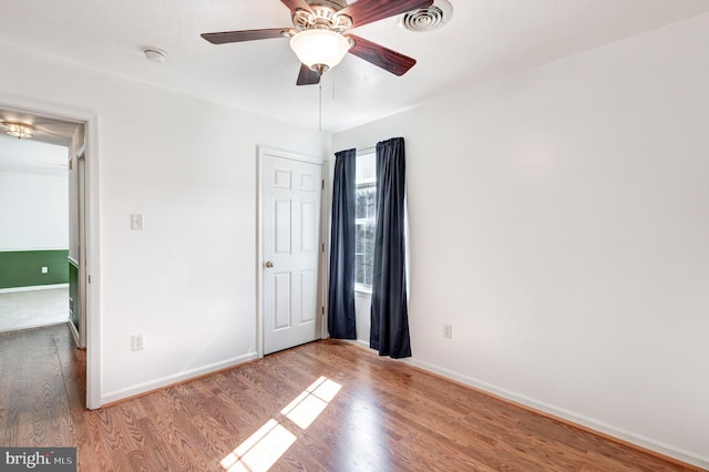 unfurnished bedroom featuring ceiling fan, visible vents, baseboards, and wood finished floors