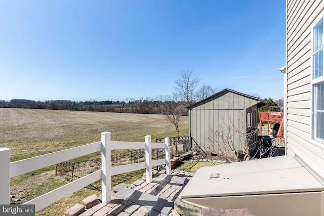 exterior space featuring an outbuilding, a rural view, a storage shed, and fence