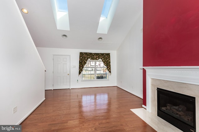 unfurnished living room with vaulted ceiling with skylight, a fireplace, baseboards, and wood finished floors