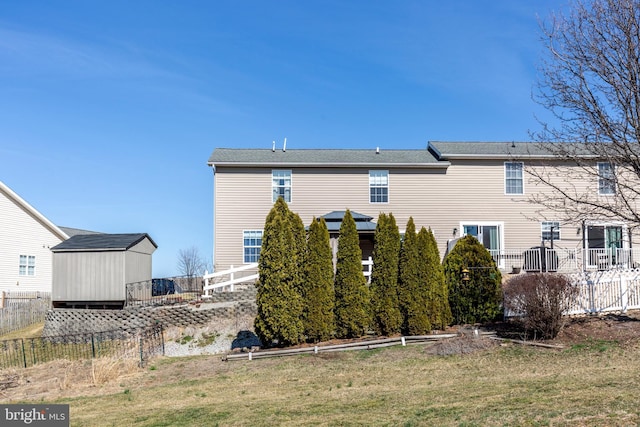 rear view of house featuring an outbuilding, a lawn, and fence