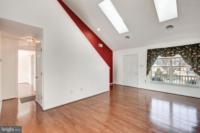 unfurnished living room with a skylight, wood finished floors, visible vents, and baseboards