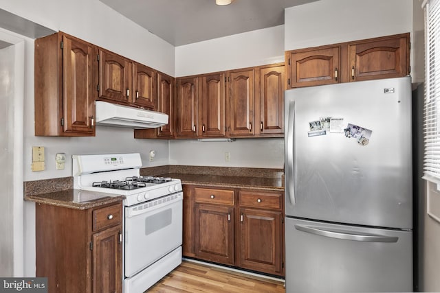 kitchen featuring light wood-style floors, freestanding refrigerator, brown cabinetry, white range with gas cooktop, and under cabinet range hood