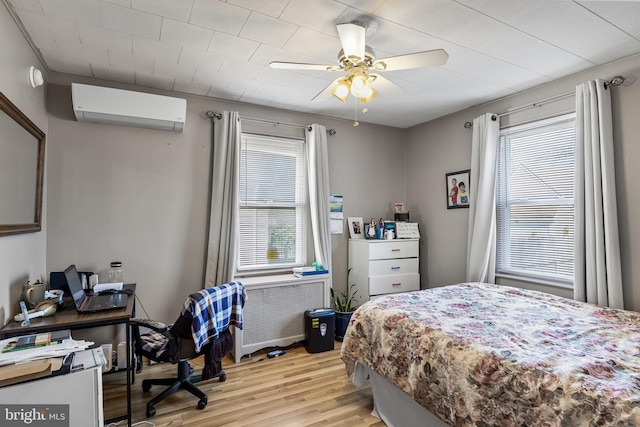 bedroom with a ceiling fan, light wood-style flooring, radiator heating unit, and a wall mounted AC