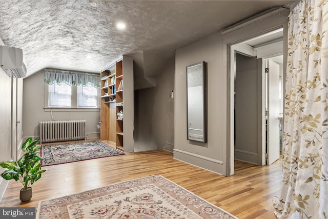 interior space with wood finished floors, a textured ceiling, radiator heating unit, and a wall mounted AC