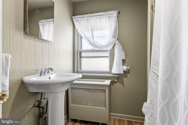 full bathroom with tile walls, a shower with shower curtain, radiator heating unit, wood finished floors, and a sink