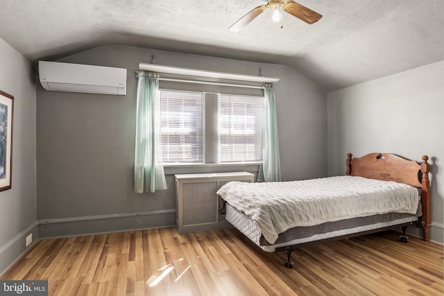 bedroom featuring a textured ceiling, a wall unit AC, wood finished floors, vaulted ceiling, and radiator