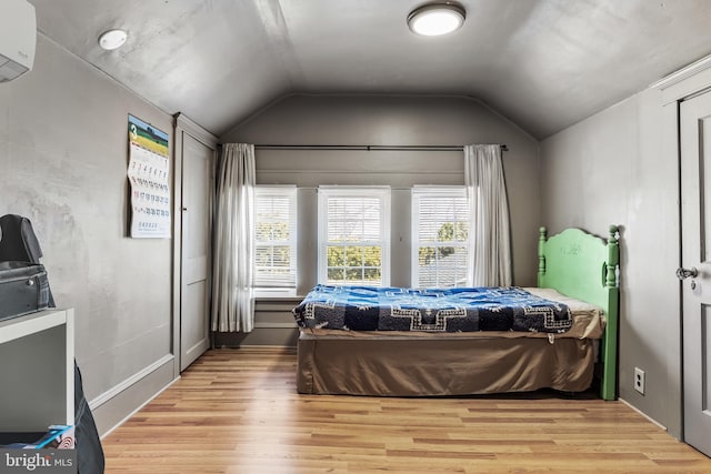 bedroom with vaulted ceiling, an AC wall unit, and light wood-type flooring