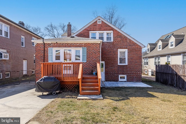 back of house featuring a chimney, fence, a lawn, and brick siding