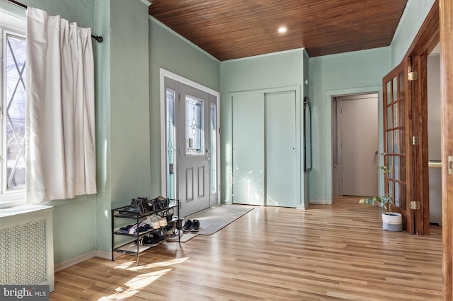 foyer entrance featuring baseboards, wood ceiling, radiator heating unit, wood finished floors, and crown molding