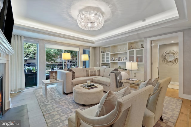 living area with a fireplace with flush hearth, a tray ceiling, light wood-style flooring, and an inviting chandelier