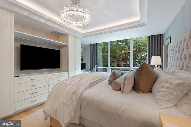 bedroom featuring a raised ceiling, visible vents, light wood-style flooring, an inviting chandelier, and expansive windows