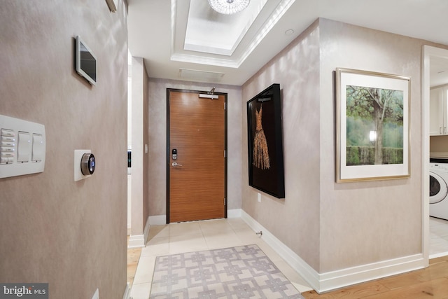 hallway featuring washer / dryer, light tile patterned floors, baseboards, a raised ceiling, and mail area