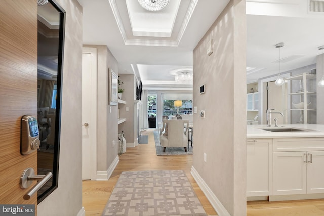 hallway featuring light wood finished floors, a raised ceiling, visible vents, a sink, and baseboards