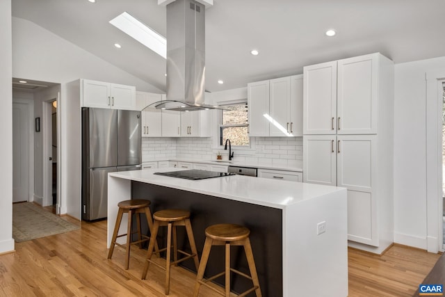 kitchen featuring island range hood, white cabinetry, appliances with stainless steel finishes, a center island, and a kitchen bar