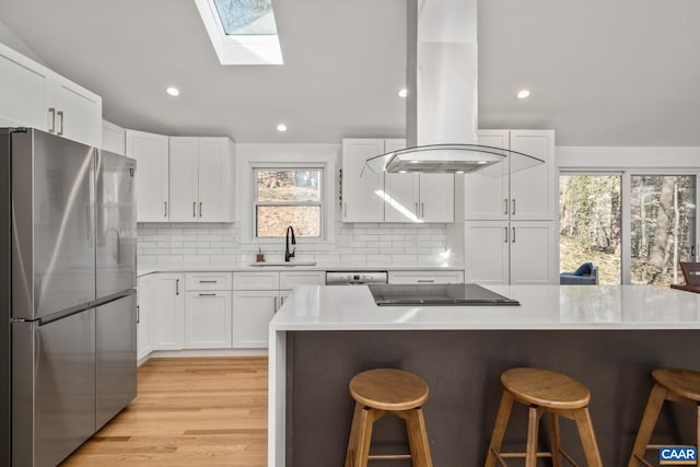 kitchen featuring a breakfast bar, a sink, white cabinetry, freestanding refrigerator, and island exhaust hood