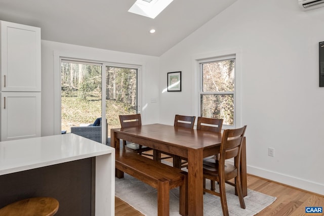 dining space with vaulted ceiling with skylight, a healthy amount of sunlight, light wood-style flooring, and baseboards