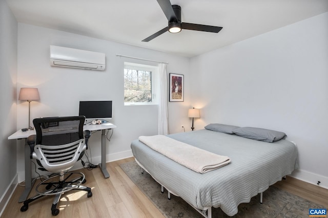 bedroom with an AC wall unit, light wood finished floors, a ceiling fan, and baseboards