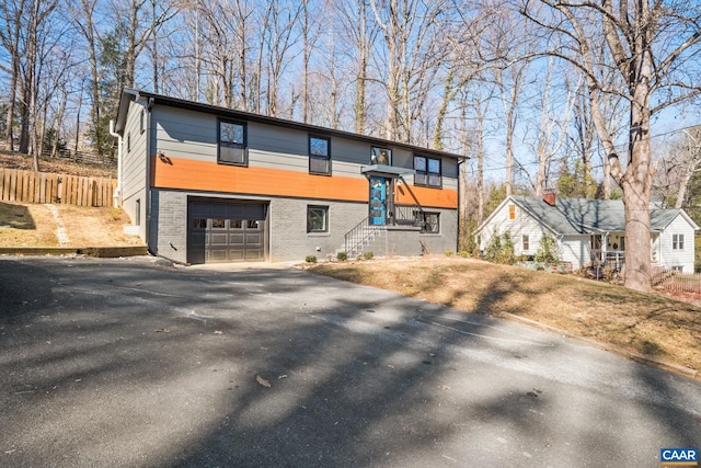 view of front of home featuring driveway, an attached garage, fence, and brick siding