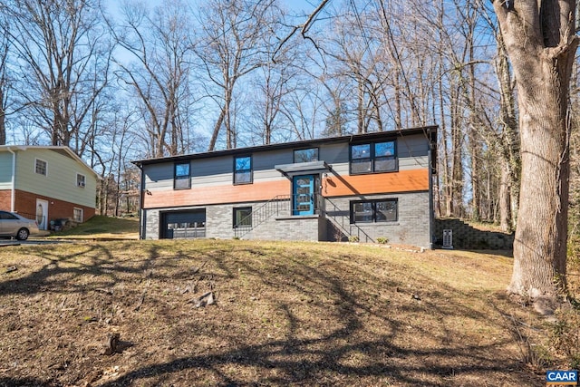 raised ranch featuring a front yard, brick siding, and an attached garage