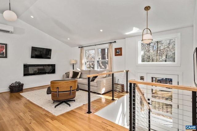 living area with a glass covered fireplace, an AC wall unit, vaulted ceiling, wood finished floors, and baseboards