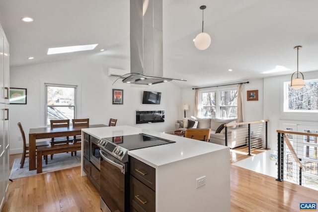 kitchen featuring vaulted ceiling with skylight, light wood-style flooring, island range hood, stainless steel range with electric cooktop, and light countertops