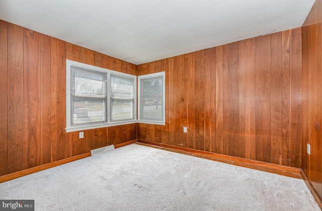 empty room featuring visible vents, wood walls, baseboards, and carpet floors