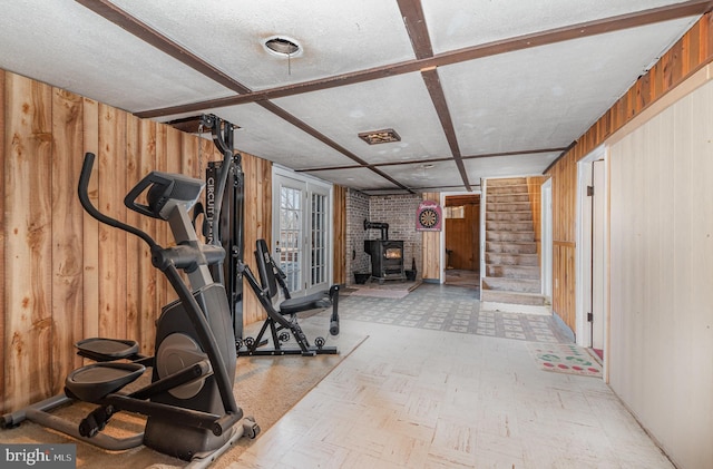 workout area featuring coffered ceiling, a wood stove, wood walls, a textured ceiling, and tile patterned floors