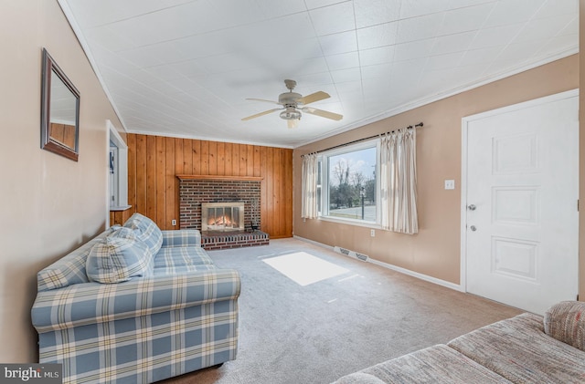 carpeted living room featuring wooden walls, visible vents, a brick fireplace, crown molding, and ceiling fan