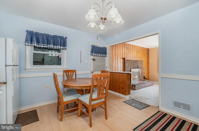 dining area featuring light wood finished floors, visible vents, a brick fireplace, baseboards, and a chandelier