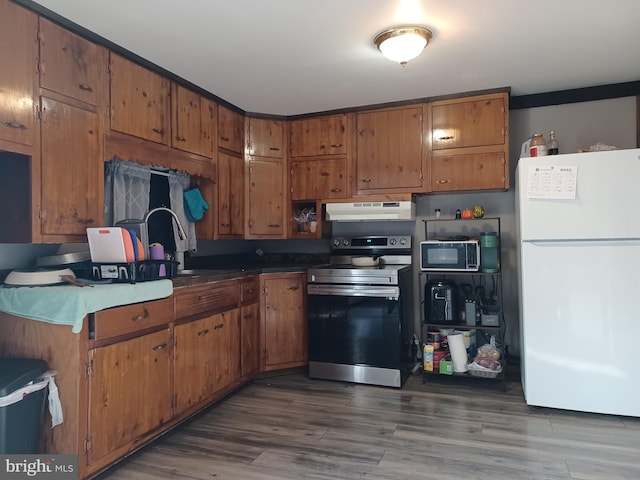 kitchen featuring under cabinet range hood, a sink, freestanding refrigerator, stainless steel electric range oven, and brown cabinetry