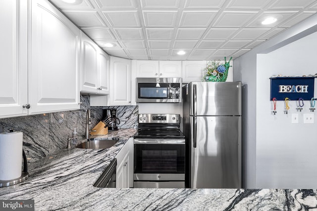 kitchen featuring light stone counters, a sink, stainless steel appliances, white cabinetry, and backsplash