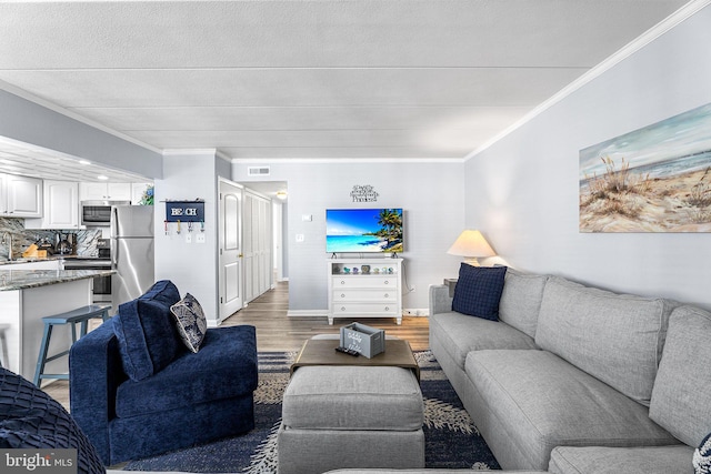 living room featuring visible vents, wood finished floors, baseboards, and ornamental molding