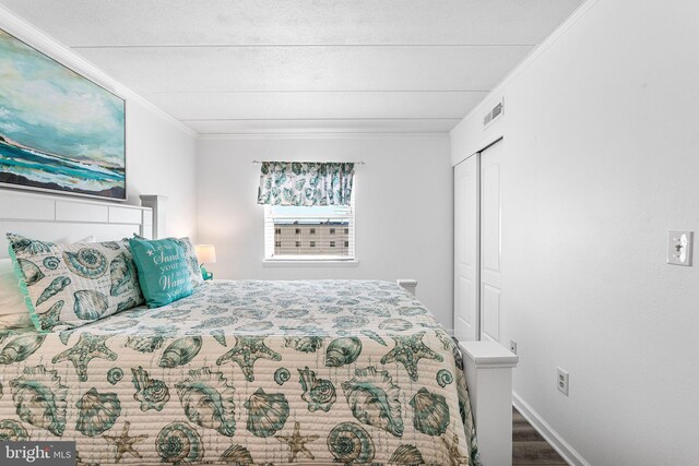 bedroom with visible vents, baseboards, ornamental molding, wood finished floors, and a closet