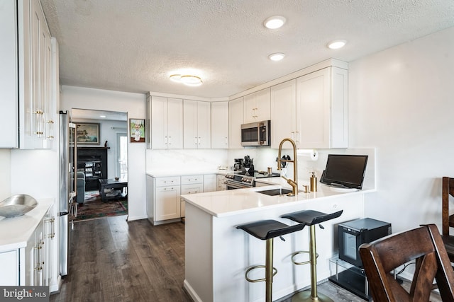 kitchen featuring dark wood finished floors, stainless steel appliances, white cabinetry, a sink, and a peninsula