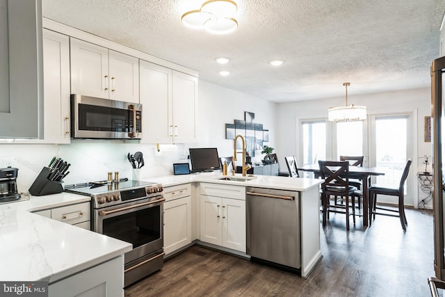 kitchen featuring dark wood-style flooring, stainless steel appliances, light countertops, a sink, and a peninsula