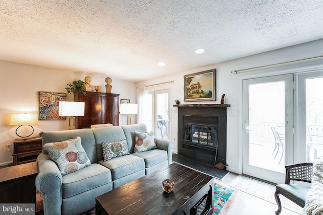 living area featuring baseboards, a fireplace with flush hearth, wood finished floors, a textured ceiling, and recessed lighting