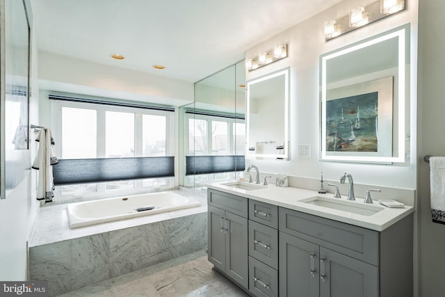 full bathroom featuring double vanity, a garden tub, marble finish floor, and a sink