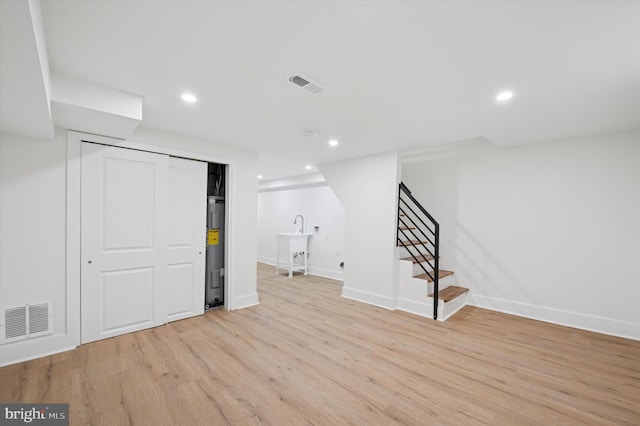 finished basement with light wood-style floors, visible vents, electric water heater, and stairs