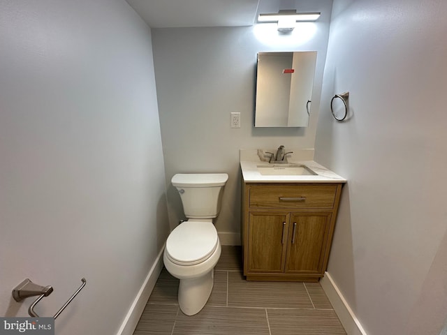 half bath featuring toilet, vanity, and baseboards