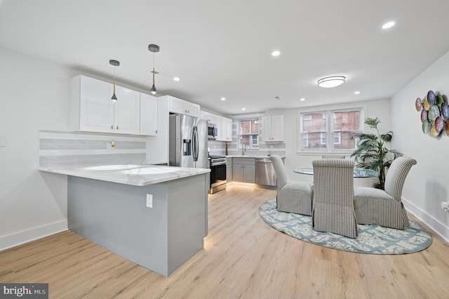 kitchen with light wood-type flooring, a peninsula, appliances with stainless steel finishes, white cabinetry, and tasteful backsplash