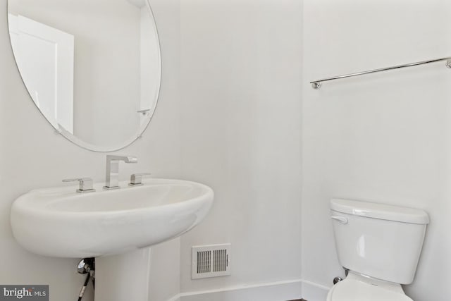 half bath with toilet, a sink, and visible vents