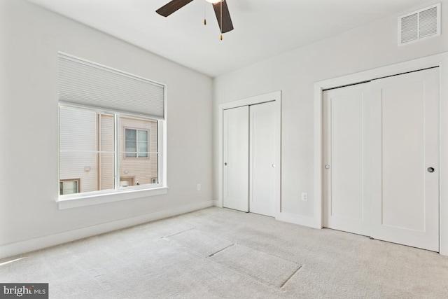 unfurnished bedroom with ceiling fan, carpet flooring, visible vents, baseboards, and two closets