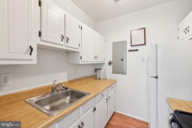 kitchen with stove, freestanding refrigerator, white cabinets, a sink, and electric panel