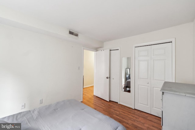 bedroom with wood finished floors, visible vents, and two closets