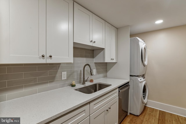 clothes washing area with light wood finished floors, baseboards, stacked washer and dryer, laundry area, and a sink