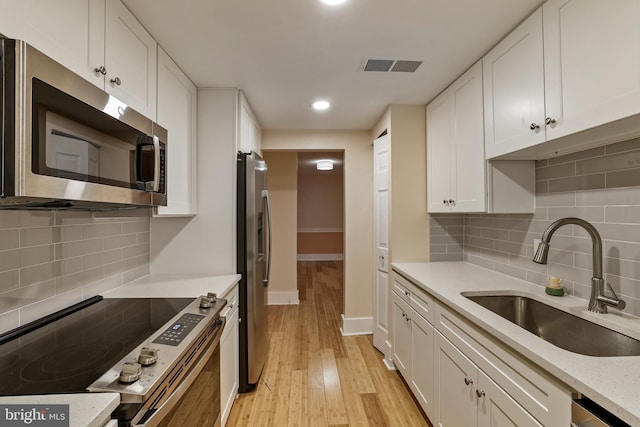 kitchen with visible vents, light wood-style flooring, appliances with stainless steel finishes, white cabinets, and a sink