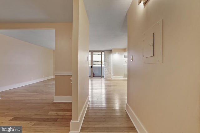 corridor featuring electric panel, baseboards, and light wood-style flooring