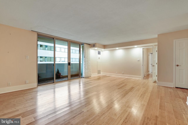 unfurnished room with light wood-type flooring, baseboards, visible vents, and expansive windows