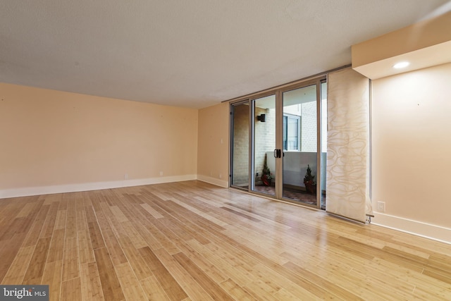 empty room featuring a wall of windows, baseboards, and light wood-style flooring